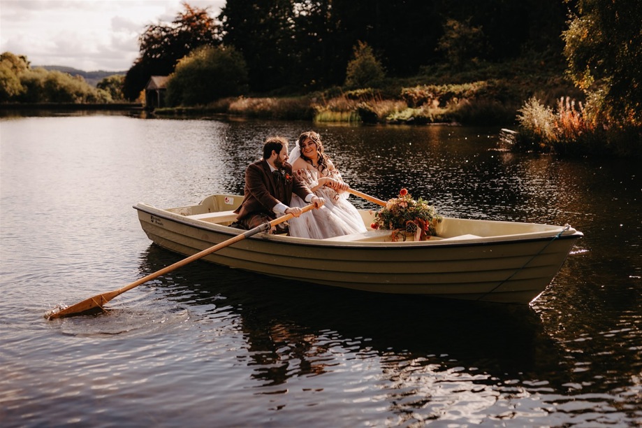 Bride and groom smile at each other in rowboat on Cardney Estate